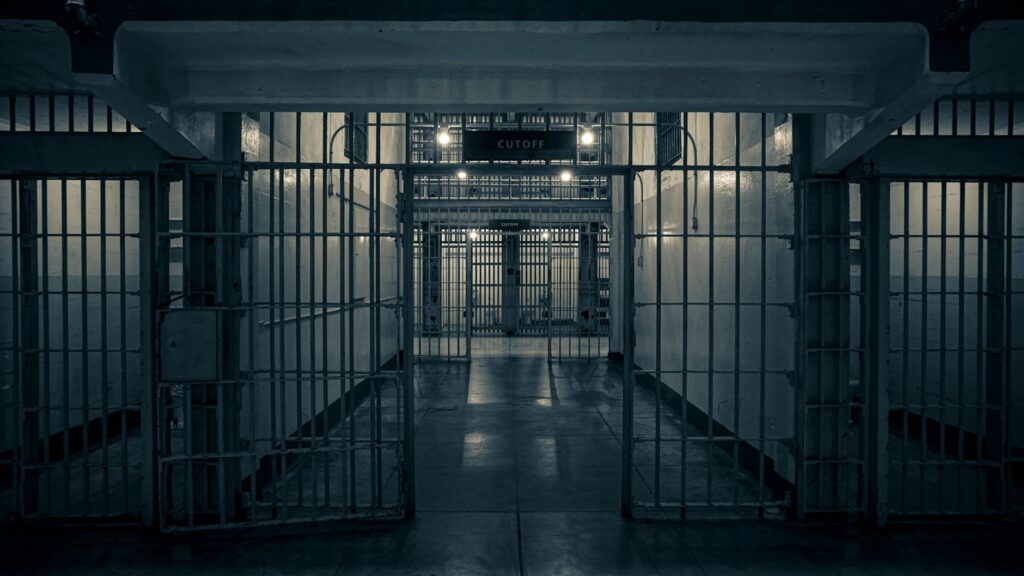 Moody interior of a prison corridor with metal bars, evoking a sense of confinement.