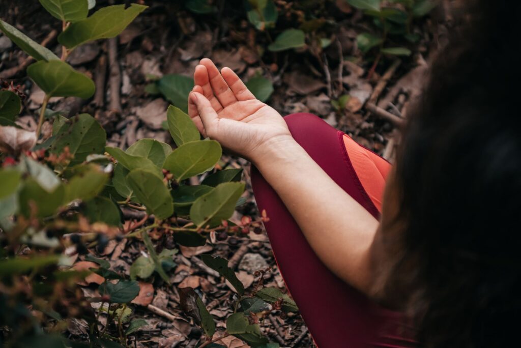 Close-up of a person meditating outdoors surrounded by green leaves, promoting relaxation and mental health.