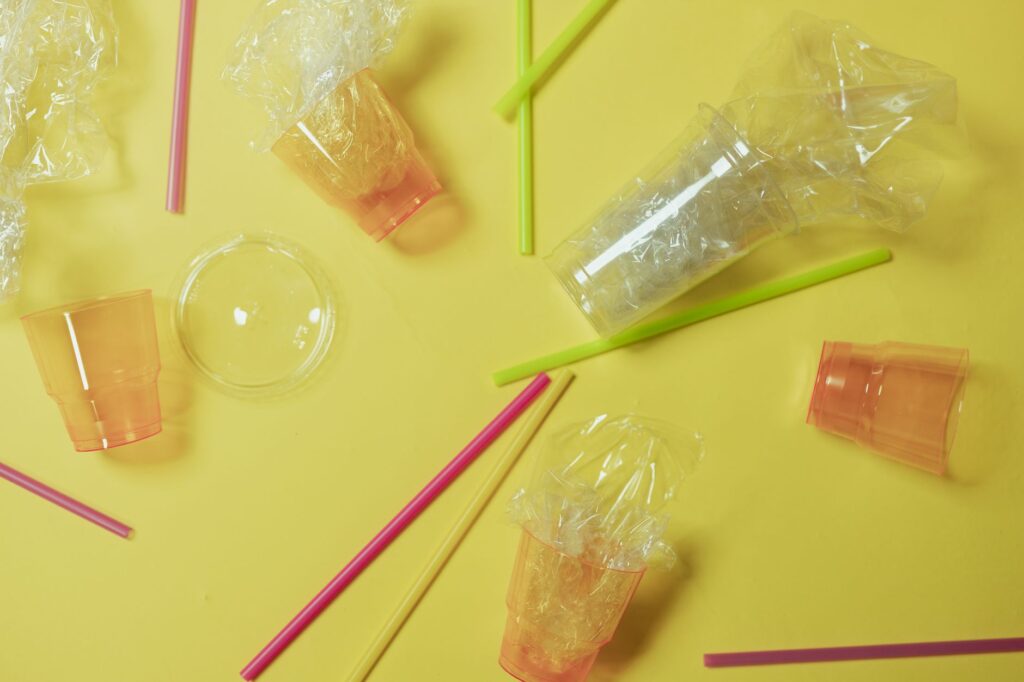 Plastic cups and straws on a yellow backdrop highlighting waste and recycling themes.